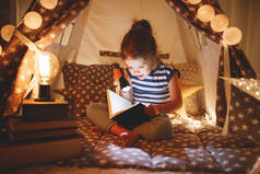 快乐的儿童女孩在黑暗的帐篷里大笑看书