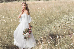 美丽的沉思年轻新娘在婚礼礼服和花卉花圈举行鲜花, 而站在户外