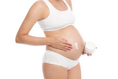 孕妇应用身体霜腹部对白色背景, 特写