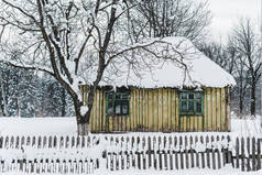 古老的风化木结构房屋与树木之间的围栏在冬季