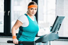 有吸引力的超重女孩在跑步机上锻炼, 而看着相机在健身房