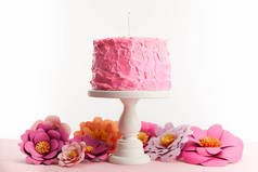 粉红色的生日蛋糕与蜡烛在蛋糕立场附近的纸花隔离在白色