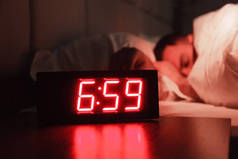 床头柜上的闹钟上有红色的数字, 睡觉的人躺在黑暗的房间里。概念厨师在餐厅辛苦一天后睡觉, 睡眠障碍, 睡过去工作, 夜班