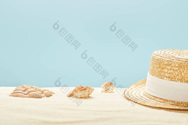 在夏季在蓝色隔离的沙滩上, 沙滩上海贝附近的草帽选择性焦点