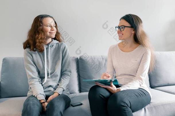 年轻女子职业心理学家与 1 4岁、1 5岁的少女坐在沙发上的办公室交谈。青春期儿童的心理健康