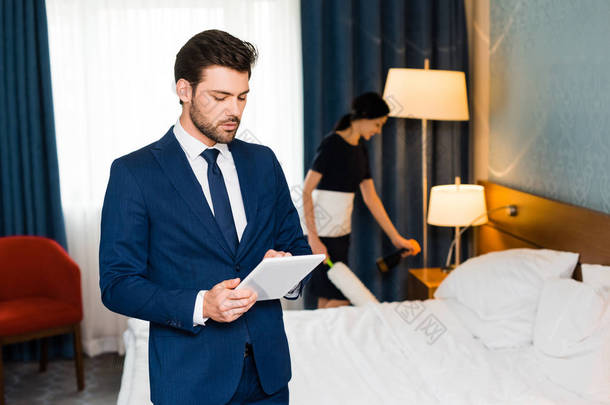选择性焦点的帅哥使用数字平板电脑附近的女佣在酒店房间