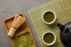 在茶壶附近的木板上用竹须配的绿色火柴粉的顶视图，在桌垫上加绿茶的白色杯子