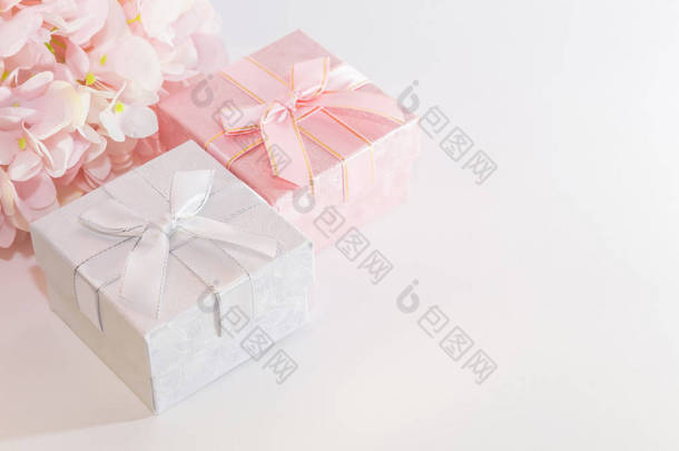 带有粉红色和银色礼品盒的贺卡的节日背景，带有蝴蝶结和人工绣球花，白色背景上柔和的颜色，带有复制空间