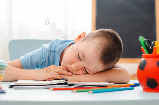 小学生坐在教室里躺着<strong>书桌</strong>，<strong>书桌</strong>里塞满了书，培训教材，小学生懒洋洋地睡着，无聊极了
