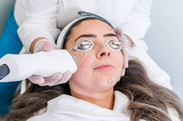 美容师在美容诊所将射频微刺手在女性面部上进行皮肤收紧治疗.