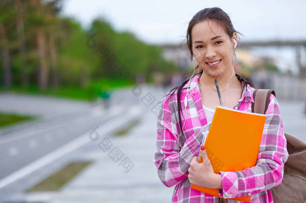 微笑的亚洲女学生与文件夹和背包在绿色的夏季公园。教育、校园和青少年观念