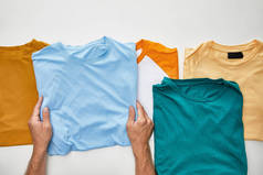 在白色背景上，手持蓝色 t-短接近米色、橙色、绿松石色和紫罗兰色的人的裁剪视图