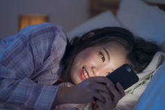young beautiful and happy sweet Asian Korean woman with in pajamas enjoying with mobile phone app in