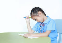 紧张的亚洲小女孩学习，厌倦了在白底的桌子上做作业。 小女孩用铅笔捂住头.