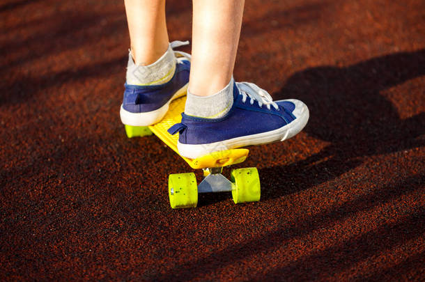 穿着蓝色运动鞋骑在活动的黄色滑板上,紧紧抓住腿. 积极的城市青年生活方式、培训、业余爱好、活动理念. 积极的儿童户外运动。 儿童滑板.