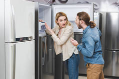 震惊的男女朋友站在家用电器店冰箱边