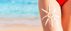 Sun shape is made of sunscreen on woman's leg at the sea backgro