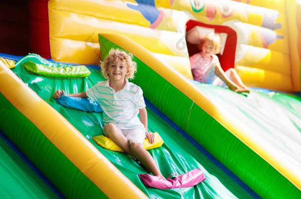 孩子跳上五颜六色的操场蹦床。孩子们跳在充气弹跳城堡在幼儿园的生日聚会活动和游乐中心的幼儿。夏天在户外玩耍的小男孩.