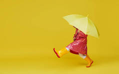 快乐的小女孩，带着黄色的雨伞，红色的雨衣，背景是黄色的。 文本的复制空间