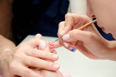 美容院的美容师在客人的指甲上涂上光亮的指甲油。在客户的指甲上画一个心脏。靠近点.
