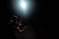 带背光的黑暗舞台上女歌手小提琴演奏的轮廓