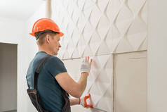 安装石膏3D面板。那位工人正在把石膏瓦贴在墙上.