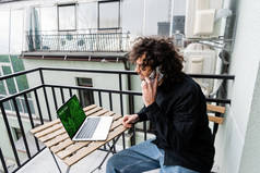 男子在笔记本电脑附近的智能手机上与在线贸易网站在阳台上交谈
