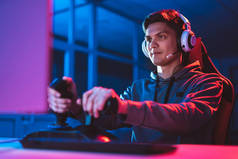 带着耳机的游戏玩家坐在霓虹灯房里玩电子游戏