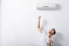 混淆不清的男人拿着遥控器，在家里用坏了的空调机取暖