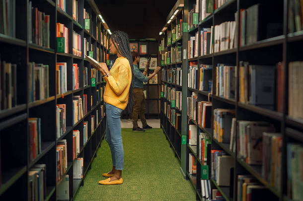 大学图书馆：在一排排书架之间挑选合适的课件的送礼的美丽的黑人女孩的镜头。以聪明学生为重点的学习、为考试而学习