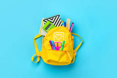 回到学校，教育理念。装有学习用品的黄色背包- -笔记本、钢笔、尺子、计算器、用蓝色背景隔开的剪刀。顶部视图。复制空间平铺构图横幅.