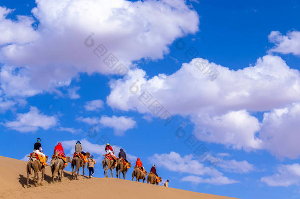 作为中国甘肃敦煌丝绸之路的一部分，成群结队的游客正在明沙山沙漠骑骆驼，或与商队一起在沙丘歌唱.