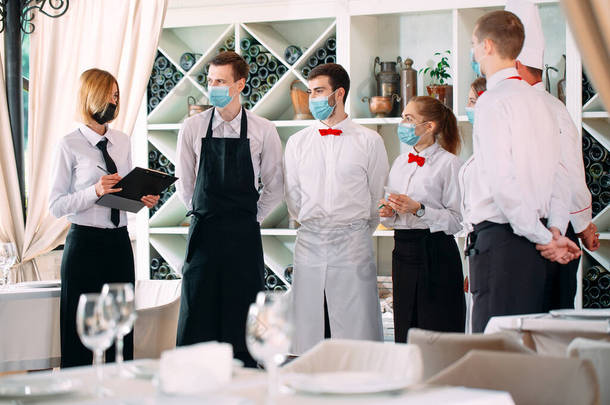 戴着防护面具的餐厅或饭店的员工。隔离的终结。餐厅经理和他的工作人员在阳台上。与餐厅厨师的互动.