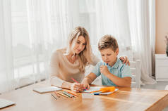 微笑的母亲帮助可爱的儿子在家里做功课