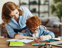 年轻妈妈帮小儿子在眼镜上做作业，一边看着儿子的笔记本，一边在网上学习