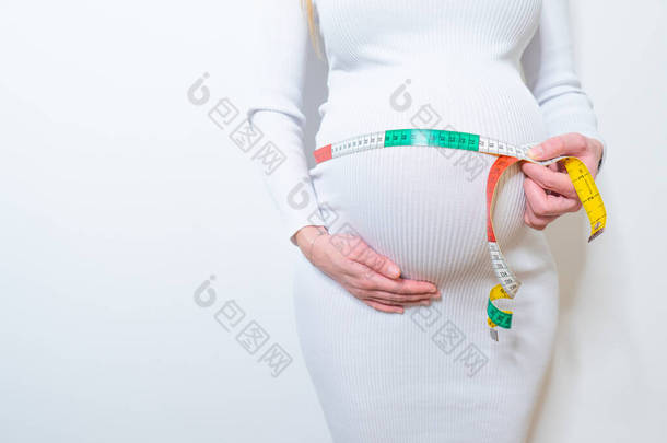 美丽的孕妇身体用测量胶带检查婴儿的发育，白色背景，健康和健康。健康福祉怀孕生活方式.