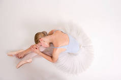 迷人的高加索女人，浅色的皮肤，金发，灰色紧身衣，尖头和白色的芭蕾舞裙躺在地板上