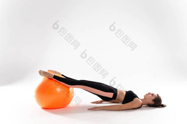一个穿着腿和运动上衣的纤细女孩躺在一个白色孤立背景的<strong>健身球</strong>上。一个有着白色背景的女运动员，带着一个<strong>健身球</strong>.