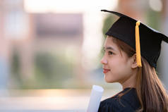 一名身穿毕业礼服的年轻快乐的亚洲女大学生在大学校园里获得了学位证书，以庆祝她的教育成就。教育库存照片
