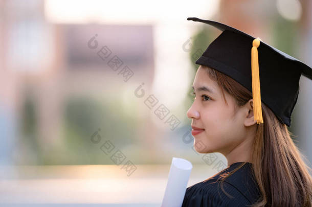 一名身穿毕业礼服的年轻快乐的亚洲女大学生在大学校园里获得了<strong>学位证</strong>书，以庆祝她的教育成就。教育库存照片