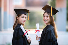 年轻快乐的亚洲女大学毕业生身着毕业礼服，身临其境，在大学校园里获得了学位证书，以庆祝她们的教育成就。教育库存照片