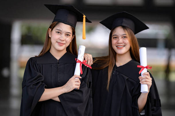 年轻快乐的亚洲女大学毕业生身着毕业礼服，身临其境，在大学校园里获得了<strong>学位证</strong>书，以庆祝她们的教育成就。教育库存照片