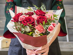 在花匠的手里，有一束红玫瑰、桉树和康乃馨。包装上的一束花。围裙上的花匠，臂膀上的花束。花店的花匠
