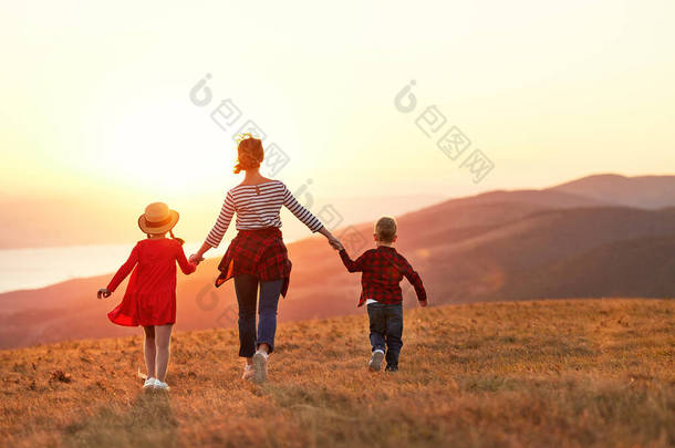 Back view of <strong>happy</strong> family: mother and two kids boy and  girl running outdoors  on sunset