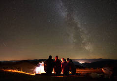 一群朋友徒步旅行者坐在一起在发光的旅游帐篷旁的篝火的后视镜