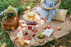 带着葡萄酒和食物在公园野餐时拿着书的年轻女子的剪影
