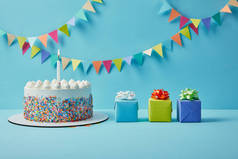 美味的蛋糕与糖洒和礼物在蓝色背景与五颜六色的地膜