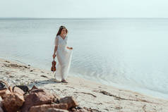 漂亮的年轻女子, 穿着优雅的连衣裙, 在海边的海滩上走着小提琴