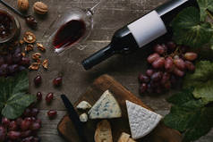 红酒瓶、杯、木桌上美味的奶酪和葡萄