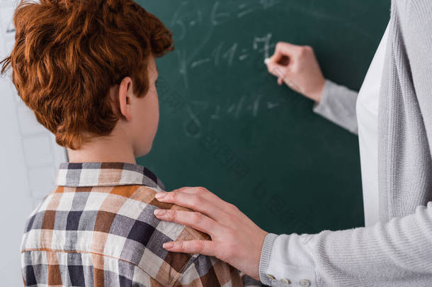 老师用模糊的背景在黑板上写字的时候摸着红头发学生的肩膀